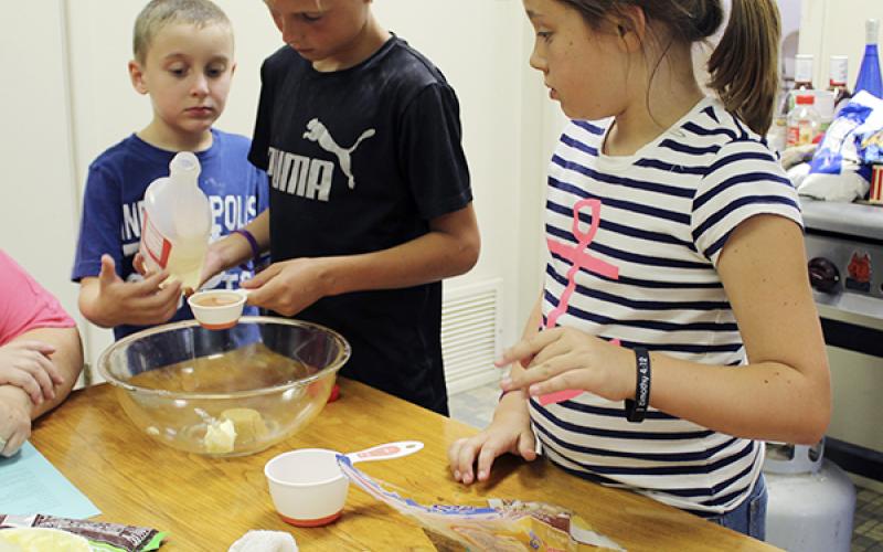 Jonathan Moser, center, measures ingrediants for sweet and salty cereal bars during the Jack County AgriLife Extension cooking camp Tuesday as Caiden Martin and Rebecca Bright look on.