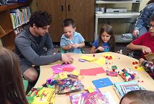 Emerson Cleghorn, center, and Brynlee Cleghorn, right, create alphabet collages during craft time led by Trey Berry, left.