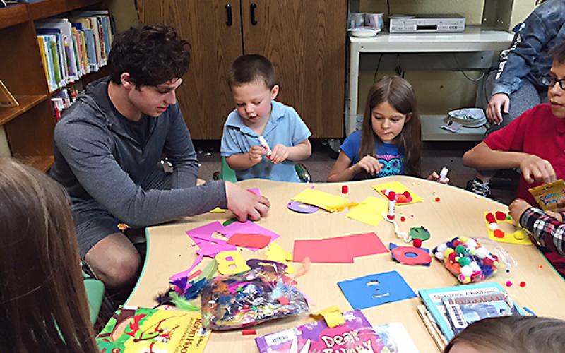 Emerson Cleghorn, center, and Brynlee Cleghorn, right, create alphabet collages during craft time led by Trey Berry, left.
