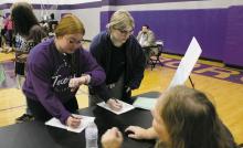 Bryson seniors Zoey Morrow, left, and Zoe Autry learn how to write a check from County Extension Agent Alinda Cox, during the Real World program held Wednesday, Feb. 22. Juniors and seniors from the county attended the program, which provides high school students information on what life will be like after graduation. Photo/Brian Smith